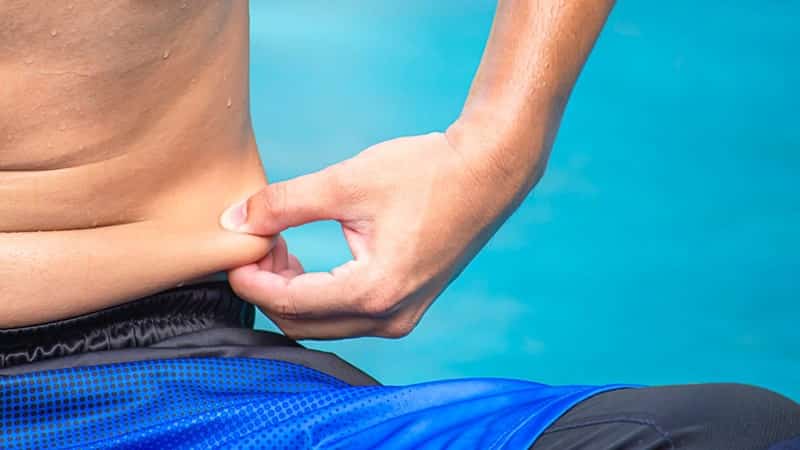 man griping skin excess fat on lower abs