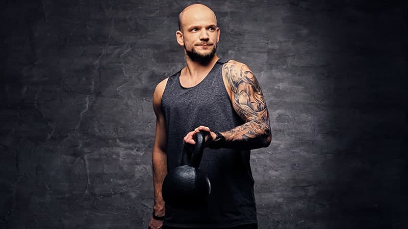 portrait of sporty tattooed shaved head male holding a kettlebell